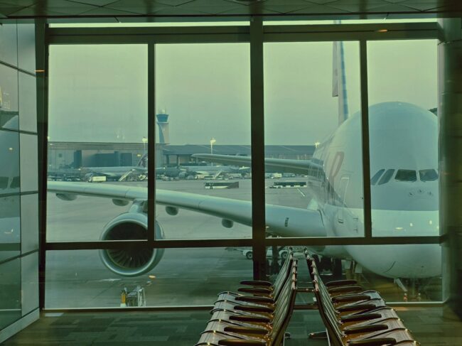 A large airplane is parked outside an airport terminal window at dawn.