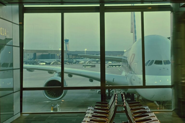 A large airplane is parked outside an airport terminal window at dawn.
